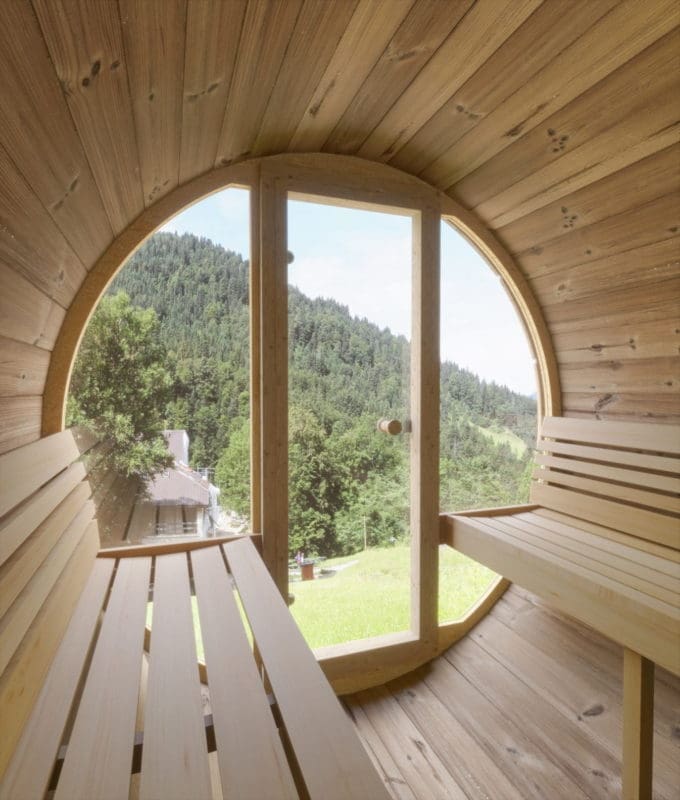 Cedar, Pine, Or Thermally Modified Nordic Spruce: The Ultimate Barrel Sauna Wood Types Showdown 2 This Image Provides A View Of A Saunalife Barrel Sauna Set Within A Garden Setting. The Sauna'S Nordic Spruce Exterior Is Beautifully Contrasting With The Green Backdrop. The Barrel Design, Shingle Roof, And The Front Door Are Prominent, Inviting Viewers To Imagine A Relaxing Sauna Experience.